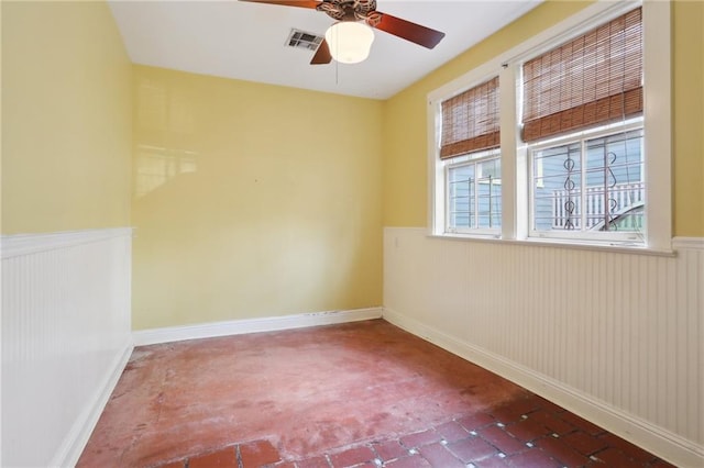 empty room with visible vents, wainscoting, and ceiling fan