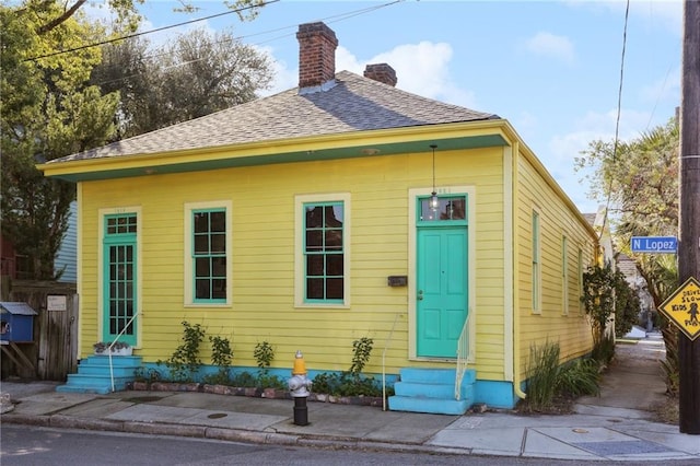 rear view of house with roof with shingles, a chimney, and entry steps