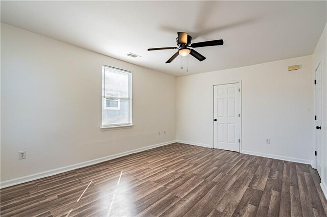 spare room featuring dark wood-style flooring, a ceiling fan, and baseboards