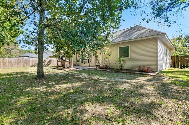 back of house featuring a fenced backyard, roof with shingles, and a yard