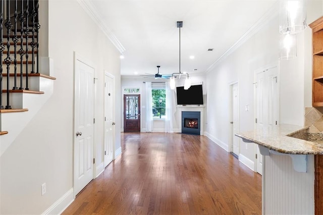 interior space with a lit fireplace, a ceiling fan, wood finished floors, and baseboards