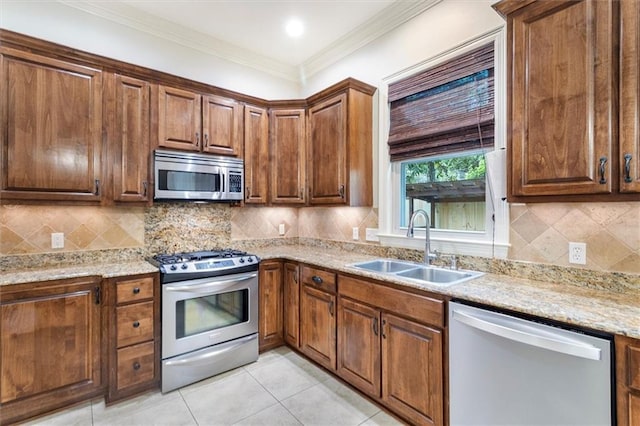 kitchen with stainless steel appliances, light stone counters, crown molding, and a sink