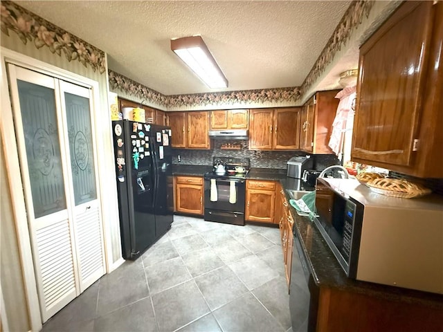 2053 Saulet Pl, Harvey, LA 70058 - kitchen with black appliances, under cabinet range hood, brown cabinetry, dark countertops, and light tile patterned flooring