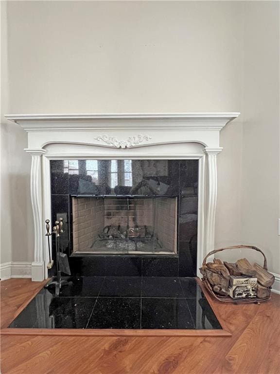 details featuring a tiled fireplace, wood finished floors, and baseboards