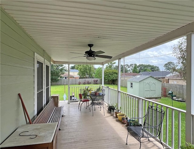 wooden terrace with an outdoor structure, a fenced backyard, a lawn, outdoor dining space, and a storage unit