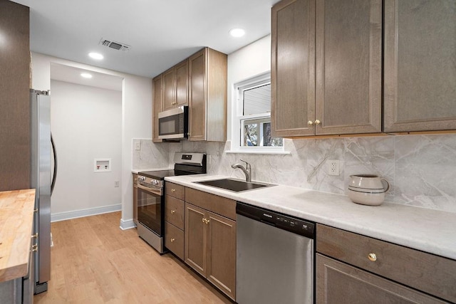 kitchen featuring light wood-style flooring, a sink, appliances with stainless steel finishes, visible vents, and baseboards