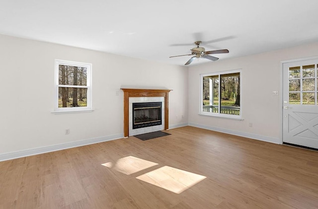 unfurnished living room with a tile fireplace, ceiling fan, wood finished floors, and baseboards