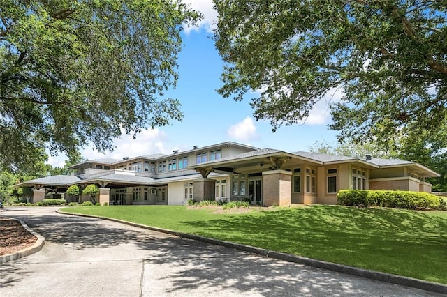 prairie-style home with brick siding, driveway, and a front lawn