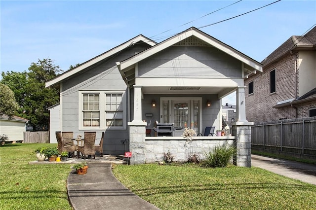 bungalow featuring a porch, a fenced front yard, and a front lawn