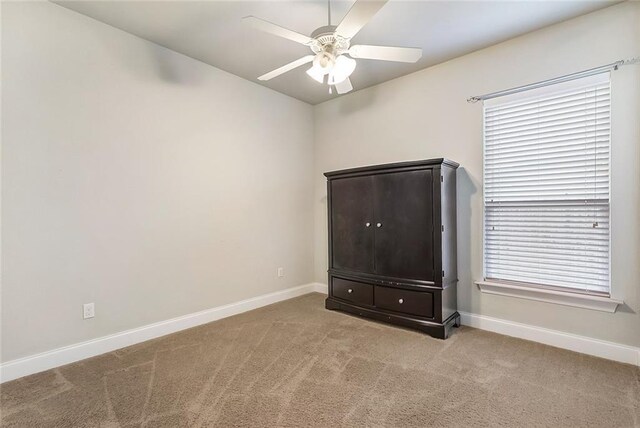 carpeted spare room featuring baseboards and a ceiling fan
