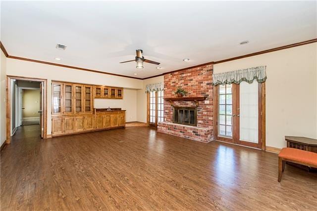 unfurnished living room with dark wood finished floors, a ceiling fan, baseboards, ornamental molding, and a brick fireplace