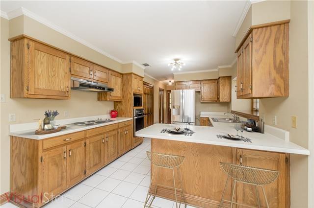 kitchen with appliances with stainless steel finishes, under cabinet range hood, a sink, a peninsula, and crown molding