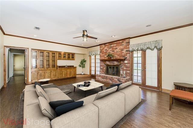 living area with wood finished floors, ornamental molding, a ceiling fan, baseboards, and a brick fireplace