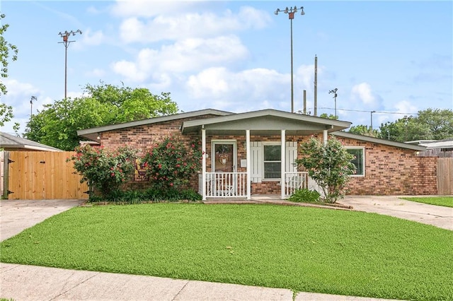 single story home with a front yard, covered porch, driveway, brick siding, and fence