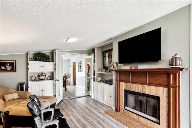 living room with a fireplace with flush hearth, a textured ceiling, ornamental molding, and light wood-style flooring