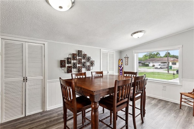 dining space featuring a textured ceiling, wood finished floors, a wainscoted wall, and vaulted ceiling