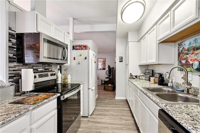 kitchen with light wood-style flooring, decorative backsplash, stainless steel appliances, white cabinets, and a sink