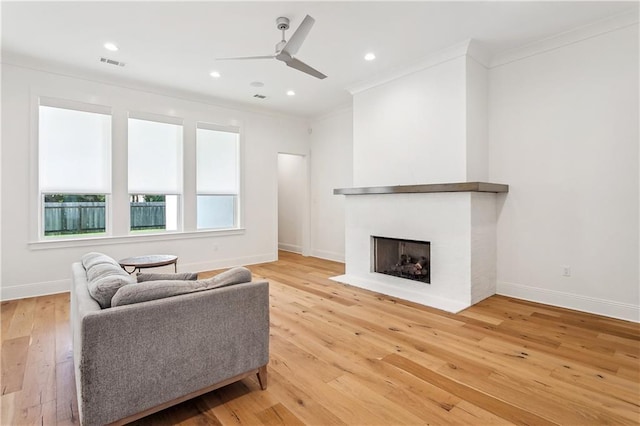 living room featuring a fireplace with flush hearth, visible vents, ornamental molding, and light wood-style floors