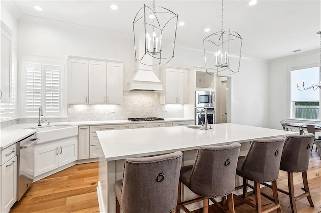 kitchen featuring a kitchen island with sink, decorative backsplash, stainless steel appliances, light countertops, and a notable chandelier