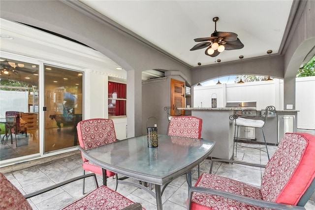 view of patio featuring fence, ceiling fan, an outdoor bar, outdoor dining area, and exterior kitchen