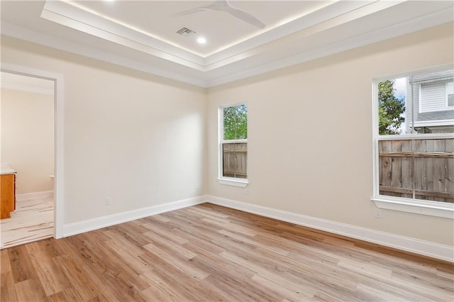 spare room featuring baseboards, a tray ceiling, visible vents, and light wood-style flooring