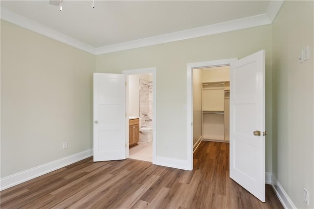 unfurnished bedroom with crown molding, baseboards, a spacious closet, and light wood-style flooring