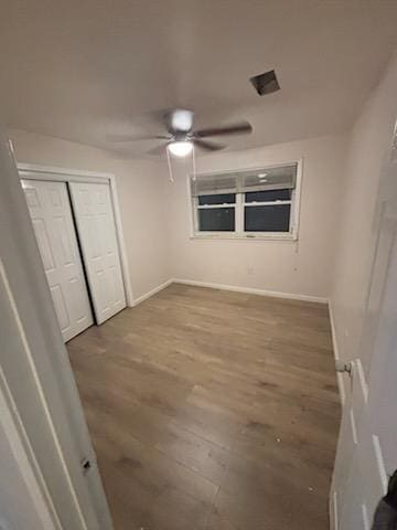 unfurnished bedroom featuring a closet, a ceiling fan, baseboards, and wood finished floors