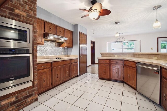 18 Landsdowne Ln, Destrehan, LA 70047 - kitchen with tasteful backsplash, brown cabinetry, stainless steel appliances, under cabinet range hood, and pendant lighting