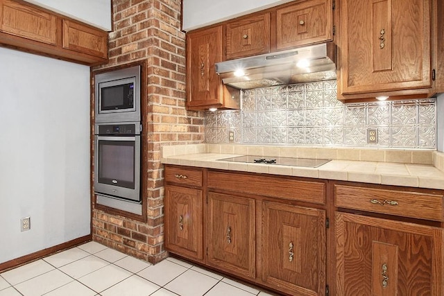 18 Landsdowne Ln, Destrehan, LA 70047 - kitchen featuring brown cabinetry, stainless steel appliances, light tile patterned floors, under cabinet range hood, and backsplash