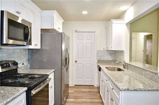kitchen with light wood-style flooring, stainless steel appliances, a sink, white cabinetry, and a peninsula