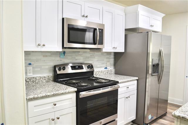 kitchen with appliances with stainless steel finishes, white cabinetry, light stone counters, and backsplash