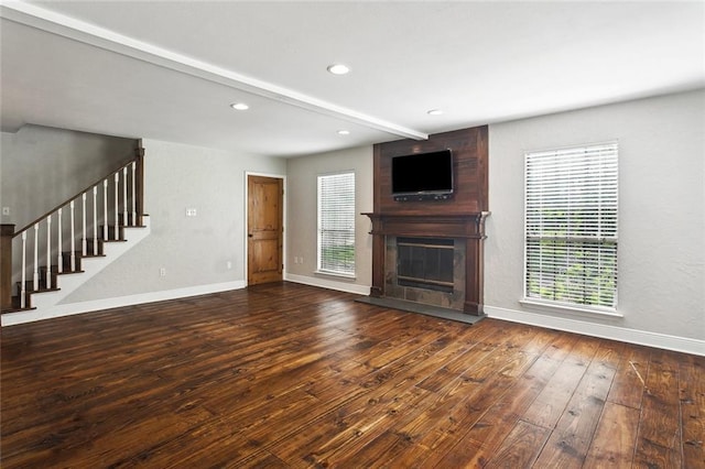 unfurnished living room featuring baseboards, stairway, a healthy amount of sunlight, and wood-type flooring