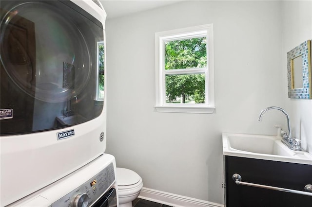 half bath featuring stacked washer and dryer, toilet, vanity, and baseboards
