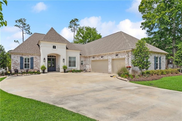 french country home featuring brick siding, driveway, roof with shingles, french doors, and an attached garage