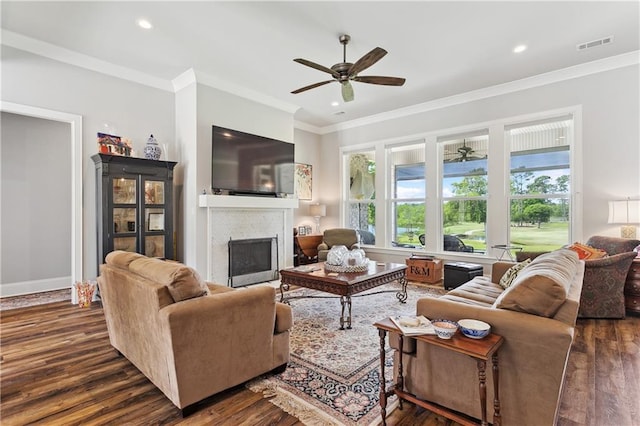 living area with ornamental molding, ceiling fan, a fireplace, visible vents, and dark wood-type flooring