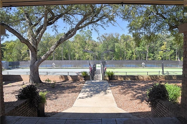 exterior space featuring a tennis court, fence, a gate, and a water view
