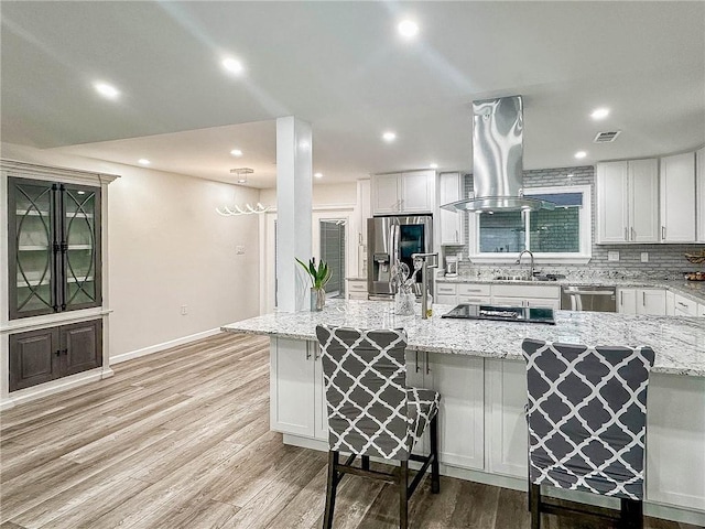 208 Bedford St, La Place, LA 70068 - kitchen with stainless steel appliances, island exhaust hood, a sink, a kitchen bar, and light wood-type flooring
