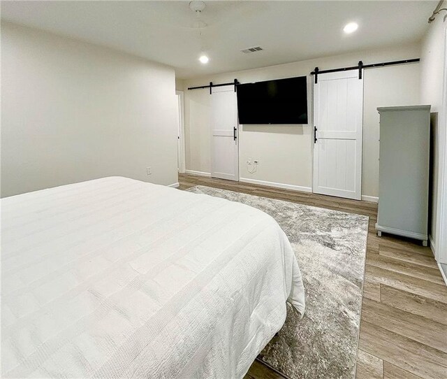 208 Bedford St, La Place, LA 70068 - bedroom with a barn door, light wood-style flooring, recessed lighting, and baseboards