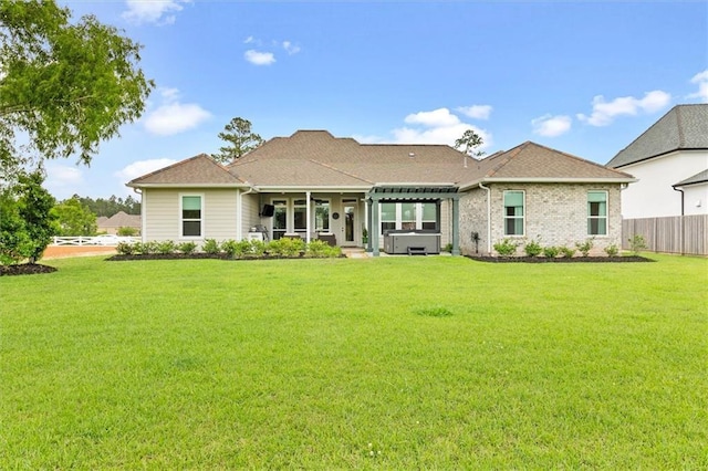 rear view of property with fence, a lawn, and a hot tub