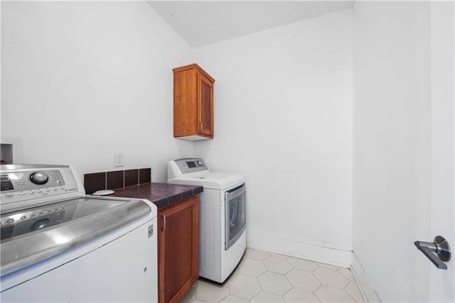 clothes washing area featuring light tile patterned flooring, washer and dryer, cabinet space, and baseboards