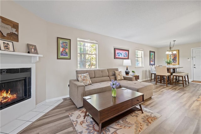 living area with a fireplace with flush hearth, an inviting chandelier, light wood-style flooring, and baseboards