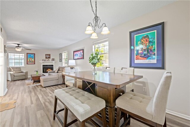 dining room with a warm lit fireplace, baseboards, a chandelier, and light wood-type flooring
