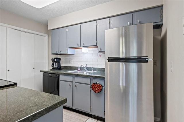 kitchen with tasteful backsplash, a sink, dark countertops, freestanding refrigerator, and dishwasher