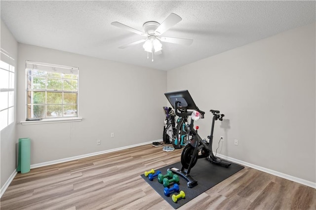 exercise room featuring a textured ceiling, wood finished floors, a ceiling fan, and baseboards