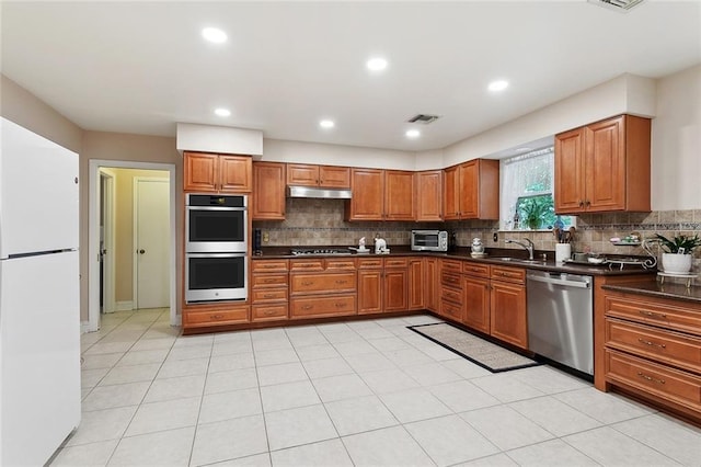 kitchen featuring dark countertops, brown cabinets, stainless steel appliances, and under cabinet range hood