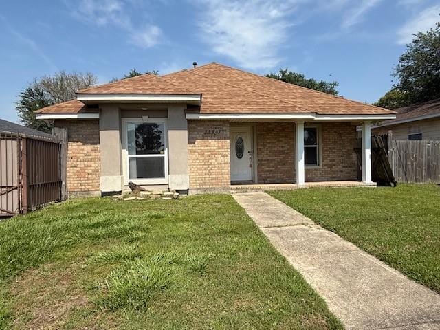 view of front of home featuring roof with shingles, brick siding, fence, a front lawn, and stucco siding