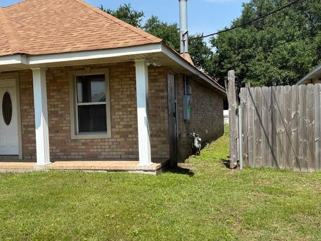 view of side of property featuring a lawn, fence, roof with shingles, and brick siding