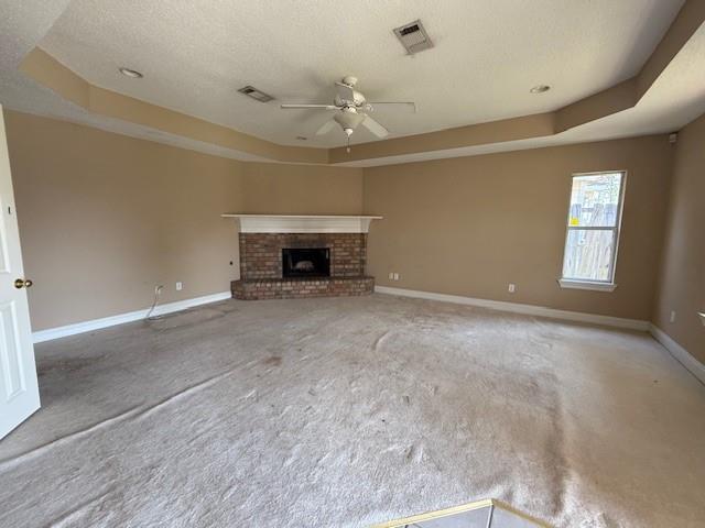 unfurnished living room with a ceiling fan, a tray ceiling, visible vents, and baseboards