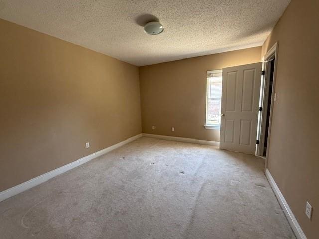unfurnished room with light colored carpet, a textured ceiling, and baseboards