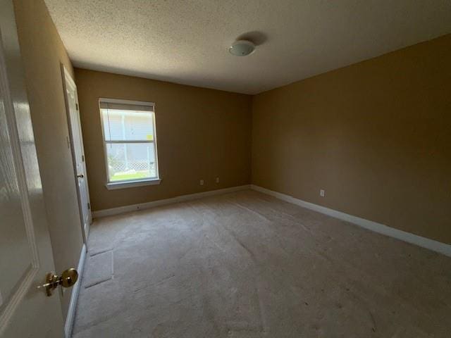 unfurnished room with a textured ceiling, baseboards, and light colored carpet
